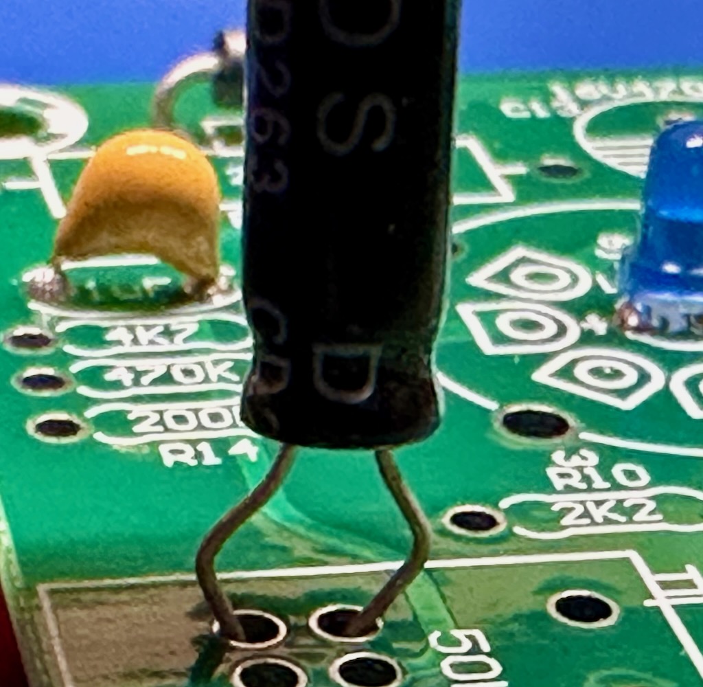 An axial electrolytic capacitor with bent leads standing off from the PCB